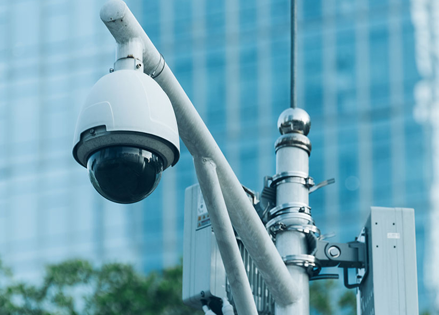 Security camera mounted on a post with a blurred city background.