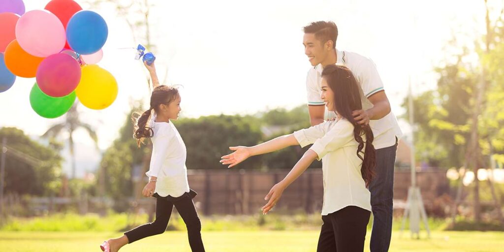 Family with colorful balloons playing outdoors in sunlight.