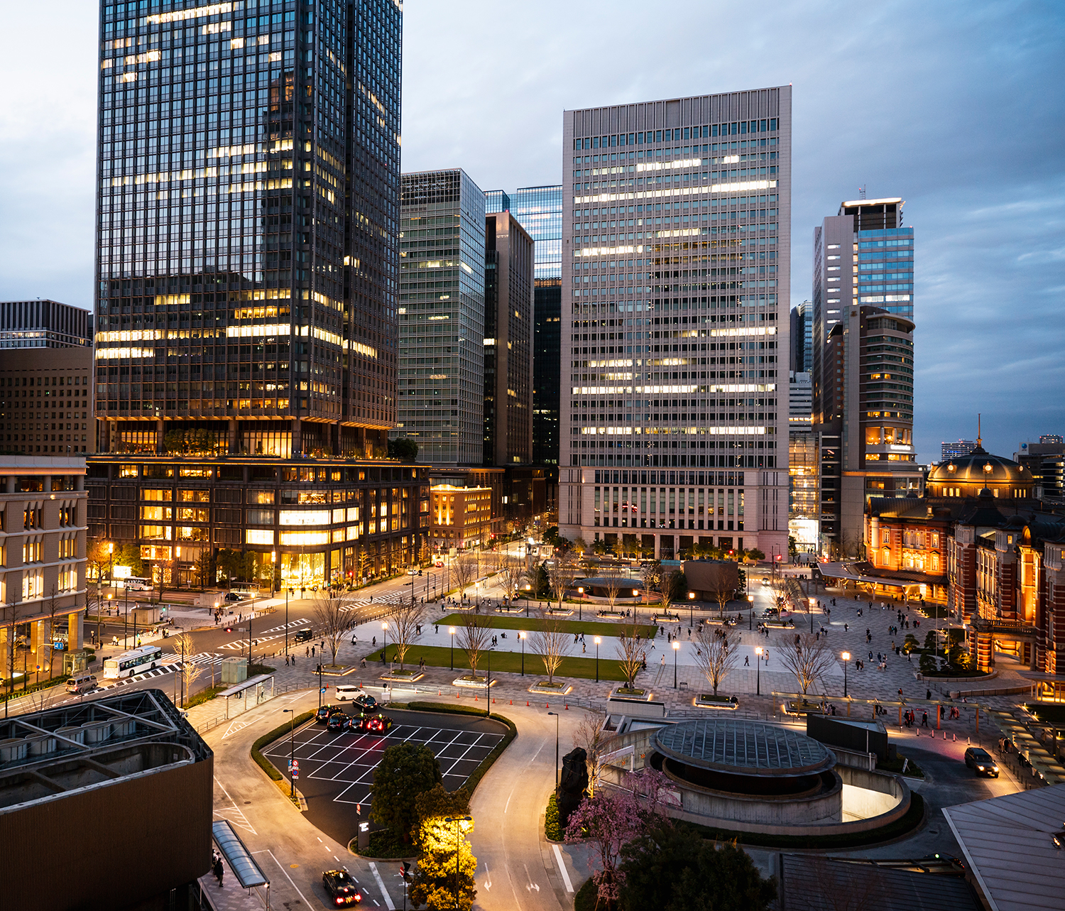 Cityscape at dusk with illuminated buildings and a bustling street.